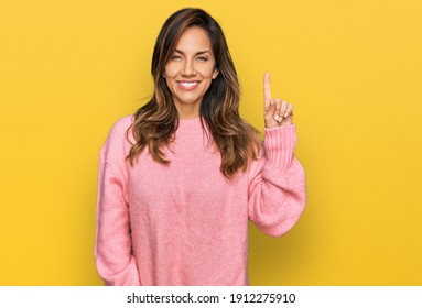 Young hispanic woman wearing casual clothes showing and pointing up with finger number one while smiling confident and happy. 
