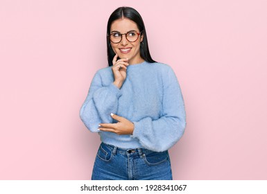 Junge hispanische Frau, die lockere Kleidung und Brille trägt, mit Hand auf dem Kinn, die über Fragen nachdenkt, pensiven Ausdruck. lächelnd mit nachdenklichem Gesicht. Zweifeln 