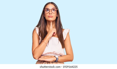 Young hispanic woman wearing casual clothes and glasses thinking concentrated about doubt with finger on chin and looking up wondering 