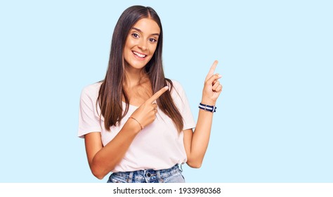 Young hispanic woman wearing casual white tshirt smiling and looking at the camera pointing with two hands and fingers to the side. 