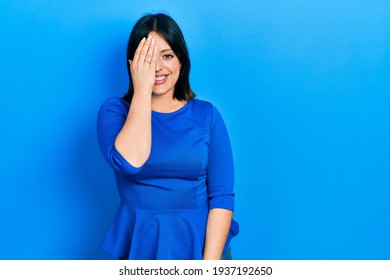 Young hispanic woman wearing casual clothes covering one eye with hand, confident smile on face and surprise emotion. 