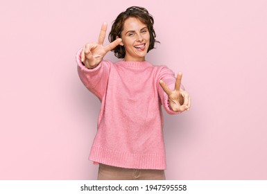 Young hispanic woman wearing casual clothes smiling with tongue out showing fingers of both hands doing victory sign. number two. 