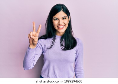 Young hispanic woman wearing casual clothes smiling looking to the camera showing fingers doing victory sign. number two. 