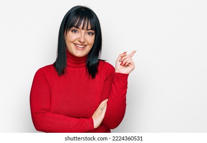 Young Hispanic Woman Wearing Casual Clothes With A Big Smile On Face, Pointing With Hand And Finger To The Side Looking At The Camera. 