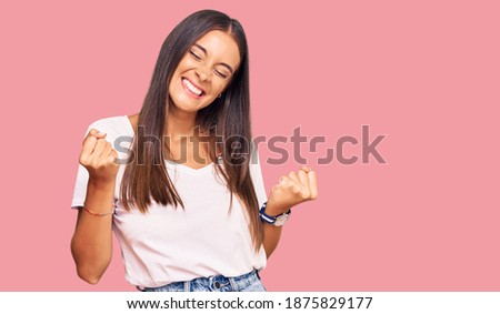 Young hispanic woman wearing casual white tshirt very happy and excited doing winner gesture with arms raised, smiling and screaming for success. celebration concept.  Foto d'archivio © 