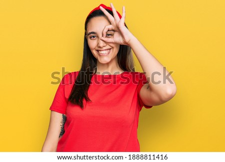 Young hispanic woman wearing casual clothes doing ok gesture with hand smiling, eye looking through fingers with happy face. 