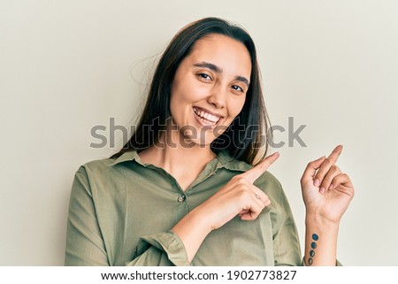 Young hispanic woman wearing casual clothes smiling and looking at the camera pointing with two hands and fingers to the side. 