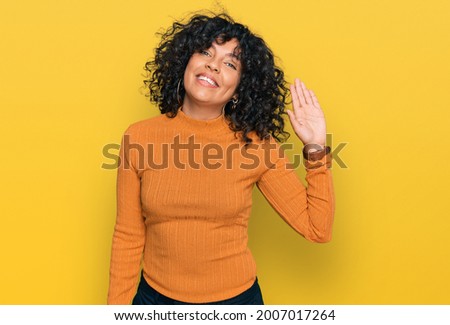 Young hispanic woman wearing casual clothes waiving saying hello happy and smiling, friendly welcome gesture 