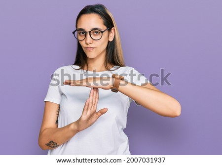 Young hispanic woman wearing casual white t shirt doing time out gesture with hands, frustrated and serious face 