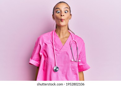 Young hispanic woman wearing doctor uniform and stethoscope making fish face with lips, crazy and comical gesture. funny expression. 