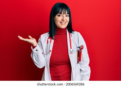 Young hispanic woman wearing doctor uniform and stethoscope smiling cheerful presenting and pointing with palm of hand looking at the camera. 