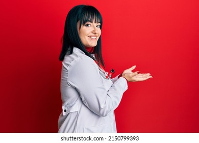 Young hispanic woman wearing doctor uniform and stethoscope pointing aside with hands open palms showing copy space, presenting advertisement smiling excited happy 