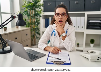 Young hispanic woman wearing doctor uniform and stethoscope looking fascinated with disbelief, surprise and amazed expression with hands on chin  - Shutterstock ID 2219169961