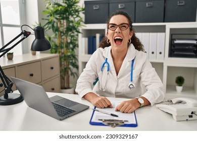 Young hispanic woman wearing doctor uniform and stethoscope angry and mad screaming frustrated and furious, shouting with anger. rage and aggressive concept.  - Shutterstock ID 2309329167