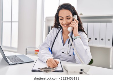 Young hispanic woman wearing doctor uniform talking on the telephone at clinic - Powered by Shutterstock