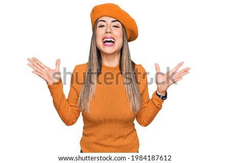 Young hispanic woman wearing french look with beret celebrating mad and crazy for success with arms raised and closed eyes screaming excited. winner concept 