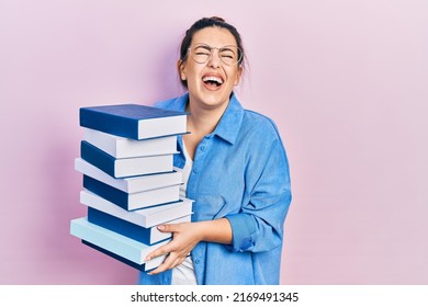 Young hispanic woman wearing glasses and holding books smiling and laughing hard out loud because funny crazy joke. 