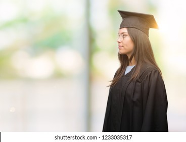 Young hispanic woman wearing graduated cap and uniform looking to side, relax profile pose with natural face with confident smile. ภาพถ่ายสต็อก