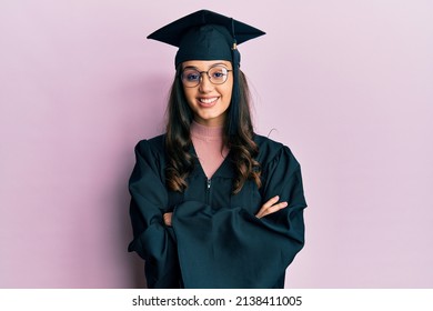 Young hispanic woman wearing graduation cap and ceremony robe happy face smiling with crossed arms looking at the camera. positive person. 
