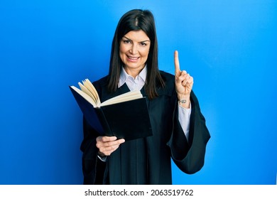 Young hispanic woman wearing judge uniform reading book smiling with an idea or question pointing finger with happy face, number one 