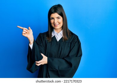 Young Hispanic Woman Wearing Judge Uniform With A Big Smile On Face, Pointing With Hand And Finger To The Side Looking At The Camera. 