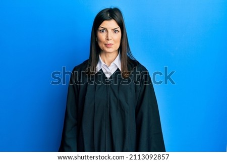 Young hispanic woman wearing judge uniform puffing cheeks with funny face. mouth inflated with air, crazy expression. 