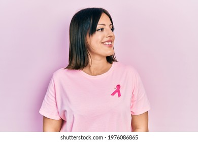 Young Hispanic Woman Wearing Pink Cancer Ribbon On T Shirt Looking Away To Side With Smile On Face, Natural Expression. Laughing Confident. 