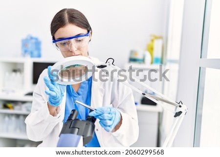 Young hispanic woman wearing scientist uniform analysing insect at laboratory