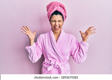 Young hispanic woman wearing shower towel cap and bathrobe celebrating mad and crazy for success with arms raised and closed eyes screaming excited. winner concept 