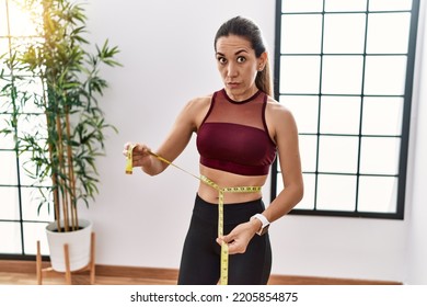 Young Hispanic Woman Wearing Sportswear Using Tape Measure At Sport Center Skeptic And Nervous, Frowning Upset Because Of Problem. Negative Person. 