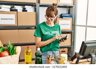 Young Hispanic Woman Wearing Volunteer Uniform Using Calculator Working At Charity Center