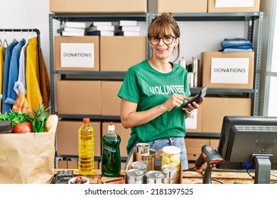 Young Hispanic Woman Wearing Volunteer Uniform Using Calculator Working At Charity Center