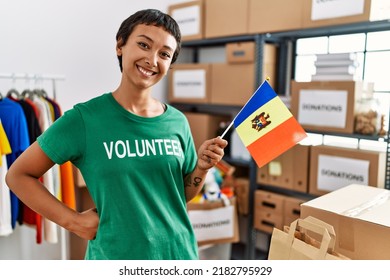 Young hispanic woman wearing volunteer uniform holding moldova flag at charity center