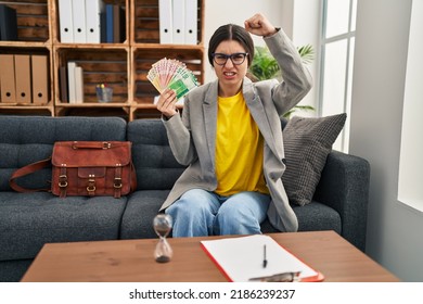 Young Hispanic Woman Working At Consultation Office Holding Money Annoyed And Frustrated Shouting With Anger, Yelling Crazy With Anger And Hand Raised 