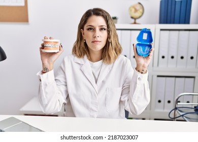 Young Hispanic Woman Working At Dentist Clinic Holding Brackets And Aligner Relaxed With Serious Expression On Face. Simple And Natural Looking At The Camera. 