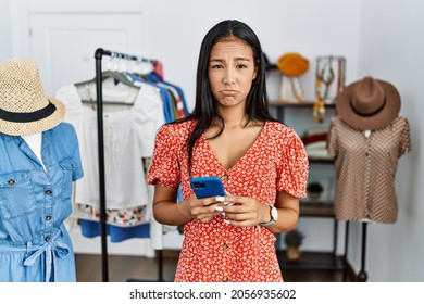 Young hispanic woman working at retail boutique using smartphone depressed and worry for distress, crying angry and afraid. sad expression. 