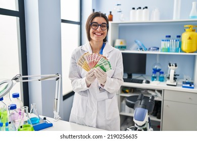 Young Hispanic Woman Working At Scientist Laboratory Holding Money Banknotes Smiling And Laughing Hard Out Loud Because Funny Crazy Joke. 