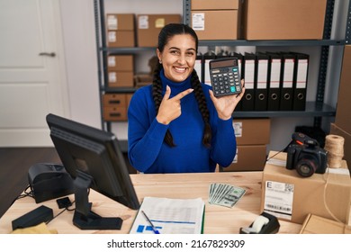 Young Hispanic Woman Working At Small Business Ecommerce Holding Calculator Smiling Happy Pointing With Hand And Finger 