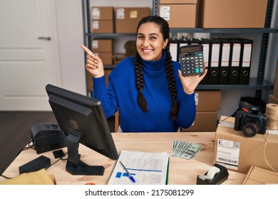 Young Hispanic Woman Working At Small Business Ecommerce Holding Calculator Smiling Happy Pointing With Hand And Finger To The Side 