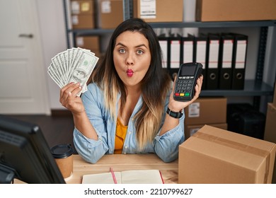 Young Hispanic Woman Working At Small Business Ecommerce Holding Money And Dataphone Making Fish Face With Mouth And Squinting Eyes, Crazy And Comical. 