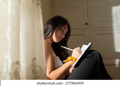 Young hispanic woman writing in a black notebook, thoughtful girl writing in her journal in her room at sunset. young man near the window concentrated studying at home.