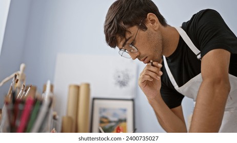 Young hispanice man, an engrossed artist, intensely thinking while drawing at the art studio, doubt and passion embodied - Powered by Shutterstock