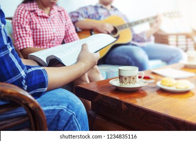 A Young  Holding Bible While His Friend Plays Guitar At Home, Christian Family, Small Group Or House Church Worship Concept