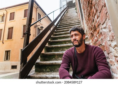 A Young Homeless Latino Immigrant Rests Bored On The Steps Of An Old European City.