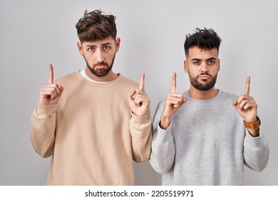 Young Homosexual Couple Standing Over White Background Pointing Up Looking Sad And Upset, Indicating Direction With Fingers, Unhappy And Depressed. 