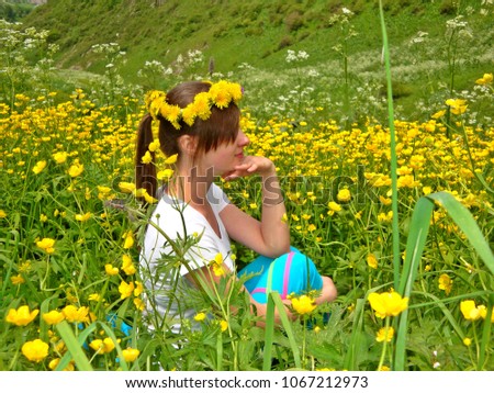 A young horny girl is sitting on the ground surrounded by yellow buttercups. She is wearing a flower wreath on her had.