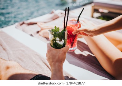 Young Hot Couple Resting At Swimpool. Picture Of Man's And Woman's Hands Holding Cocktails. Cool Drink With Ice Inside Glass. Enjoy Summer Vacation At Swimming Pool. Resort Spa Place.