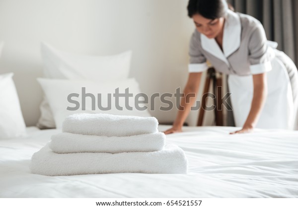 Young\
hotel maid making the bed with clean fresh\
towels