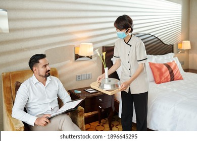 Young Hotel Maid In Medical Mask Bringing Tray With Breakfast To Room Of Businessman