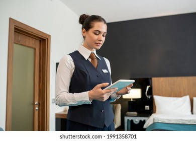 Young Hotel Worker In Uniform Using Tablet In Bedroom